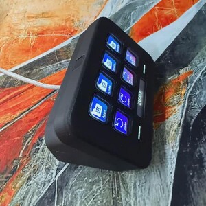 May include: A black electronic control panel with several illuminated buttons. The buttons show icons and text such as "Apps", "Links", and "Undo". The device has a rectangular shape and is connected to a white cable.