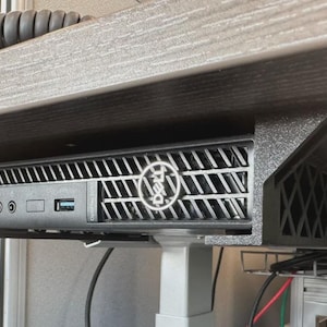 May include: A black Dell OptiPlex computer mounted under a wooden desk. The computer has a silver Dell logo and various ports. The mounting bracket is grey.
