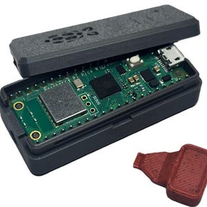 May include: A black rectangular electronic device with a green circuit board inside. The device is open, revealing the internal components. A small, red, rectangular piece sits next to the device. The top of the device has the text "333".