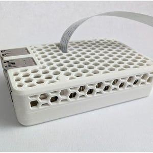 May include: A white, rectangular electronic device with a honeycomb pattern on the top and sides. It has two USB ports and a flat, grey ribbon cable extending from the top. The device appears to be a computer component.