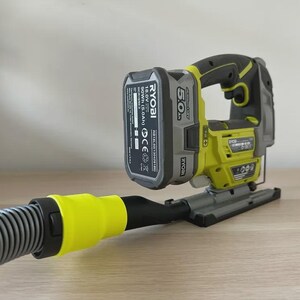 May include: A cordless Ryobi jigsaw in black and yellow, connected to a vacuum hose. The power tool has a battery pack and is placed on a wooden surface.