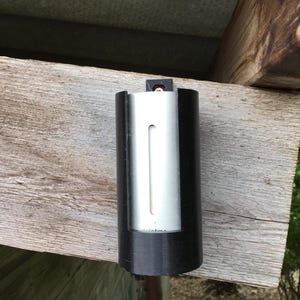 May include: A black and silver cylindrical object with a rectangular opening, mounted on a wooden surface. The text "totme" is visible on the silver section of the object.