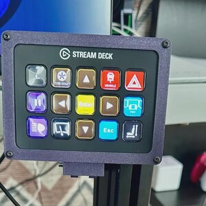May include: A Stream Deck control panel with multiple illuminated buttons. The panel has a dark purple frame and features icons for various functions, including vehicle, POV, and tyre reset. The text "STREAM DECK" is visible at the top.
