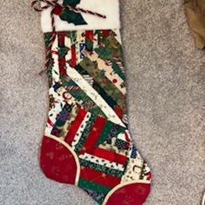 May include: A Christmas stocking made of patchwork fabric with a red, green, and white color scheme. The stocking has a white cuff with a green holly leaf and red berries.