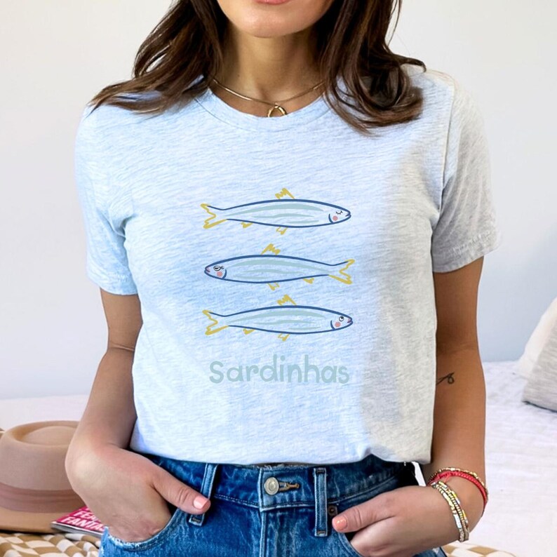 Cute Sardines T-Shirt displayed in a flat lay style, featuring a playful Portuguese sardine art design. This funny fish tee has a coastal aesthetic, perfect for seafood lovers and beachgoers. Shown on a soft, high-quality fabric with a relaxed fit.
