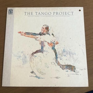 May include: Album cover for "The Tango Project" featuring a watercolor painting of a dancing couple. The album title and artist names are printed in black. The artwork depicts a man in a suit and a woman in a white dress, with a splash of blue and brown.