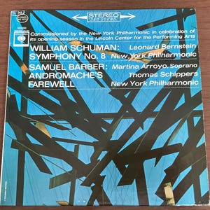 Puede incluir: Una portada de álbum de vinilo vintage con un diseño abstracto azul y negro. El álbum presenta la Sinfonía n.º 8 de William Schuman y el Adiós de Andrómaca de Samuel Barber, interpretados por la Filarmónica de Nueva York.