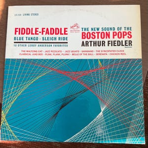 May include: Vintage vinyl record album cover for "Fiddle-Faddle" by The Boston Pops, featuring Arthur Fiedler. The cover has a teal background with red, yellow, and white geometric lines. The album title and artist's name are in red and white.