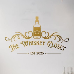 May include: Gold vinyl wall decal featuring the words "The Whiskey Closet" with a whiskey bottle illustration and decorative flourishes. The text "EST 2025" is below the main text. The decal is displayed on a white wall.