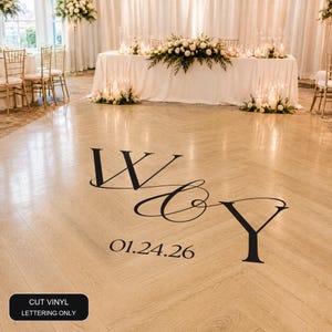 May include: A black vinyl decal applied to a light wood herringbone floor, featuring the large stylised letters W and Y connected by an ampersand, with the date 01.24.26 printed below in a serif font. The text CUT VINYL LETTERING ONLY is visible.