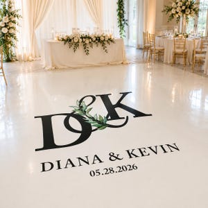 Peut inclure: Un sol de réception de mariage blanc avec un grand monogramme noir des lettres "D&K" entrelacées avec un motif de feuilles vertes. Le texte "DIANA & KEVIN" et la date "05.28.2026" sont en dessous. L'arrière-plan présente des tables, des chaises et des compositions florales.