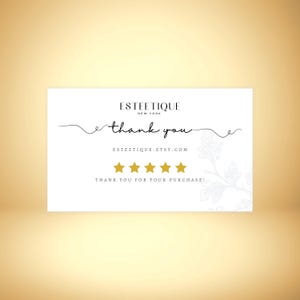 May include: A white thank you card with the text "ESTEETIQUE NEW YORK" at the top. The words "thank you" are written in cursive. Below are five gold stars and the text "THANK YOU FOR YOUR PURCHASE!"