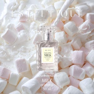 Op de afbeelding: Een parfumflesje met een helder, rechthoekig ontwerp en een kristalachtige dop. Het etiket luidt "ESTEETIQUE MARSHMALLOW MILK PERFUME 30 ml". Het flesje is omgeven door witte en roze marshmallows in een melkachtige vloeistof.