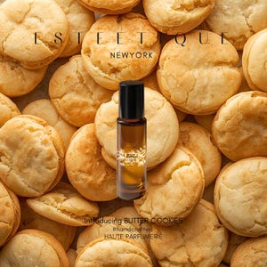 May include: A perfume bottle with a black cap sits among a pile of golden-brown butter cookies. The bottle is filled with a light brown liquid. The text "Introducing BUTTER COOKIES" and "#handcrafted HAUTE PARFUMERIE" is visible.