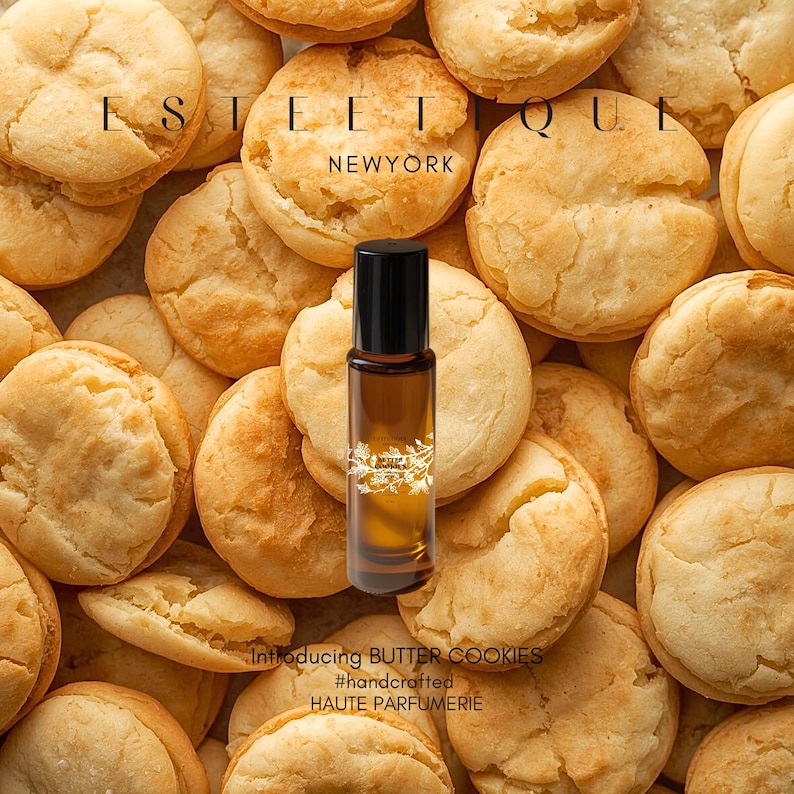 May include: A perfume bottle with a black cap sits among a pile of golden-brown butter cookies. The bottle is filled with a light brown liquid. The text "Introducing BUTTER COOKIES" and "#handcrafted HAUTE PARFUMERIE" is visible.
