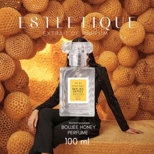 May include: A clear perfume bottle with a square shape and a clear, decorative top. The label reads "ESTEETIQUE BOUJEE HONEY PERFUME 100 ml." The background features a honeycomb pattern and the text "ESTEETIQUE EXTRAIT DE PARFUM."
