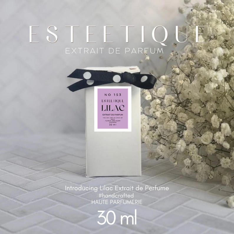 Puede incluir: Una caja de perfume blanca con un lazo de lunares blanco y negro. La caja tiene una etiqueta lila con el texto "LILAC" y "EXTRAIT DE PARFUM". Tambi&eacute;n se ve el texto "Introducing Lilac Extrait de Perfume". El frasco contiene 30 ml de perfume.