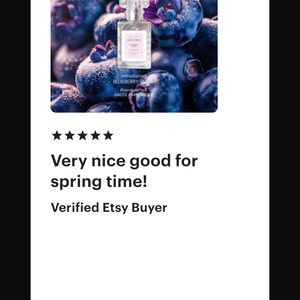 May include: A perfume bottle with a clear cap and a pink label, set against a backdrop of fresh blueberries and purple flowers. The text on the label reads "BLUEBERRY SUGAR".