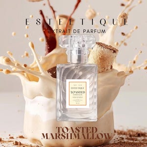 Puede incluir: Un frasco de perfume rectangular transparente con una tapa plateada está centrado en un chorro de líquido color crema. El frasco tiene una etiqueta que dice "ESTETIQUE TOASTED MARSHMALLOW". El fondo presenta salpicaduras de chocolate y trozos de malvavisco.