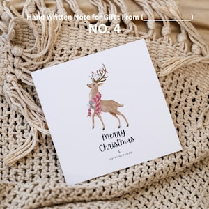 May include: A white greeting card with a watercolor illustration of a reindeer wearing a scarf. The card reads "Merry Christmas & Happy New Year." The card is on a beige knitted blanket. Text at the top reads "Hand Written Note for Gift: From ( ) NO. 4."