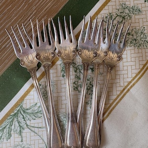 Puede incluir: Seis tenedores antiguos de plata con detalles ornamentales en los mangos y dientes. Los tenedores están colocados sobre un mantel estampado con detalles verdes y dorados. Un clásico para cualquier juego de comedor.