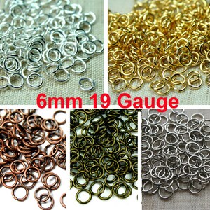 May include: A close-up image of a large quantity of 6mm jump rings in four different colors: silver, gold, bronze, and antique brass. The jump rings are 19 gauge.