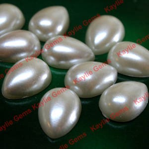 May include: A group of ten white pearlescent teardrop-shaped cabochons. The cabochons are smooth and glossy.