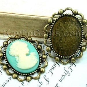 Peut inclure: Deux cadres de camée en métal doré antique avec des détails ornés. Un cadre présente un fond bleu clair avec une silhouette de camée blanche d'un profil de femme. L'autre cadre est vide.