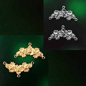 May include: Two gold-toned metal floral embellishments with three loops on each side. The embellishments are shaped like a half-circle and feature a design of stylized flowers.