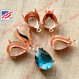 Puede incluir: Cinco engastes de metal en tono oro rosa para piedras preciosas en forma de lágrima, con un engaste que contiene una piedra preciosa en forma de lágrima azul. Hecho en los EE. UU.