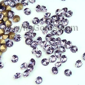 May include: A scattering of small, round, purple rhinestones on a white surface. The rhinestones have a faceted design and a shiny finish.