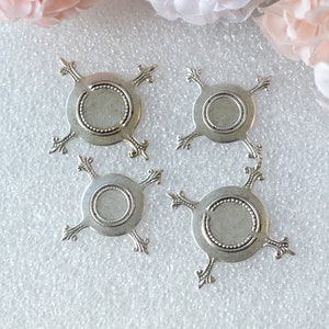 May include: Four silver-toned metal embellishments with a circular design and four points. Each embellishment has a raised, beaded border around the centre circle.