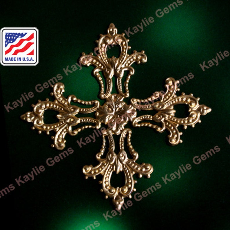 May include: Gold-toned metal cross with a decorative, ornate design. The cross has a filigree pattern with small, round accents. The cross is on a green background.