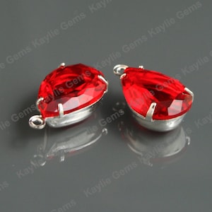 May include: Two red teardrop-shaped crystal rhinestones with silver settings and loops for hanging.