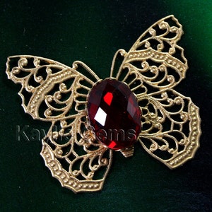 May include: Gold filigree butterfly with a red faceted gem in the center.