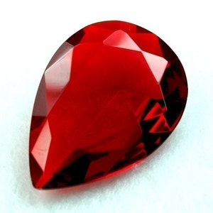 May include: A teardrop-shaped, faceted, red gemstone.