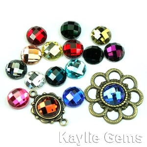 Puede incluir: Surtido de piedras de cristal redondas y facetadas en varios colores, incluyendo rojo, verde, azul, dorado, plateado y negro. Las piedras están dispuestas sobre una superficie blanca. También hay una pieza de metal decorativa con una piedra de cristal azul en el centro.
