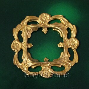 May include: Gold-toned metal frame with a square opening and intricate floral designs. The frame is ornate and has a vintage aesthetic.