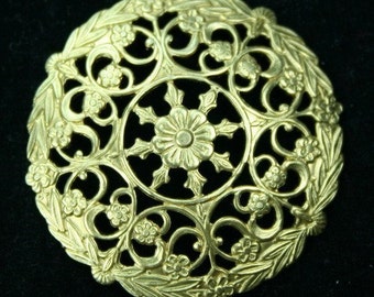 May include: A gold-toned metal filigree ornament with a circular design featuring intricate floral patterns and leaves.