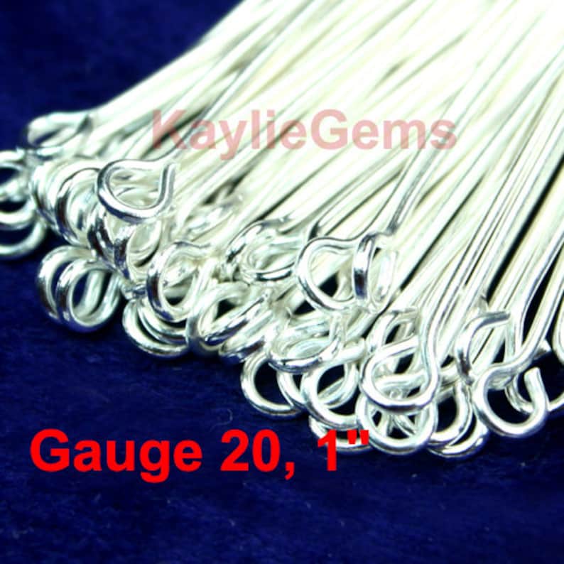 May include: A close-up of a pile of silver jump rings, each with a small loop at one end. The rings are 1 inch long and 20 gauge. The text "Gauge 20, 1" is visible in the image.
