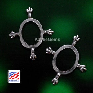 May include: Two silver metal oval-shaped rings with four decorative points on each ring. The rings are on a green background.  Made in U.S.A.