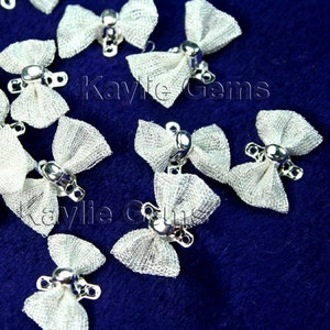 May include: A close-up of a group of white tulle bows with silver metal clasps. The bows are scattered on a blue fabric surface.