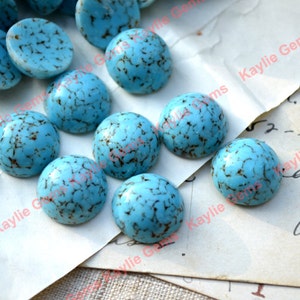 Op de afbeelding: Een verzameling van 12 turquoise cabochons met bruine adering. De cabochons zijn rond en hebben een glad, gepolijst oppervlak. Ze zijn ongeveer 2,5 cm in diameter.