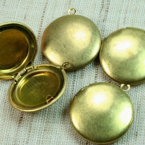 May include: Four gold-toned metal locket pendants with hinged lids. The lockets are round and have a smooth, polished finish.