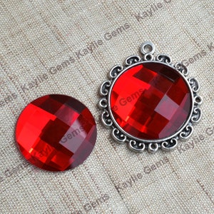 May include: Two red glass cabochons with a faceted design. One cabochon is set in a silver-toned metal pendant with a decorative border.