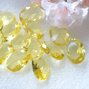 May include: A group of yellow oval-shaped faceted glass beads. The beads are scattered on a white surface.