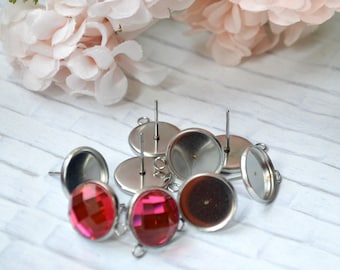 May include: A set of six silver earring settings with a round, flat base and a post for attaching earrings. Two of the settings have red, faceted gems attached.
