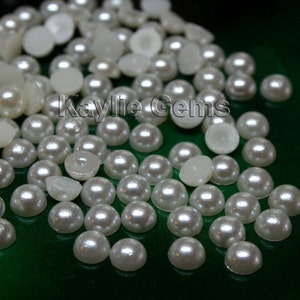 May include: A close-up image of a large quantity of white pearl-like round buttons. The buttons are scattered on a green surface.