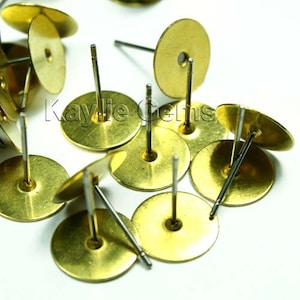 Puede incluir: Primer plano de un montón de postes de pendientes de color dorado con respaldos redondos. Los postes son de metal y tienen un acabado liso.