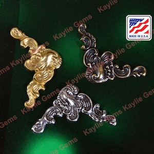 May include: Three ornate metal corner brackets in gold, silver, and black. The brackets are decorative and have a scroll-like design.  Made in the U.S.A.